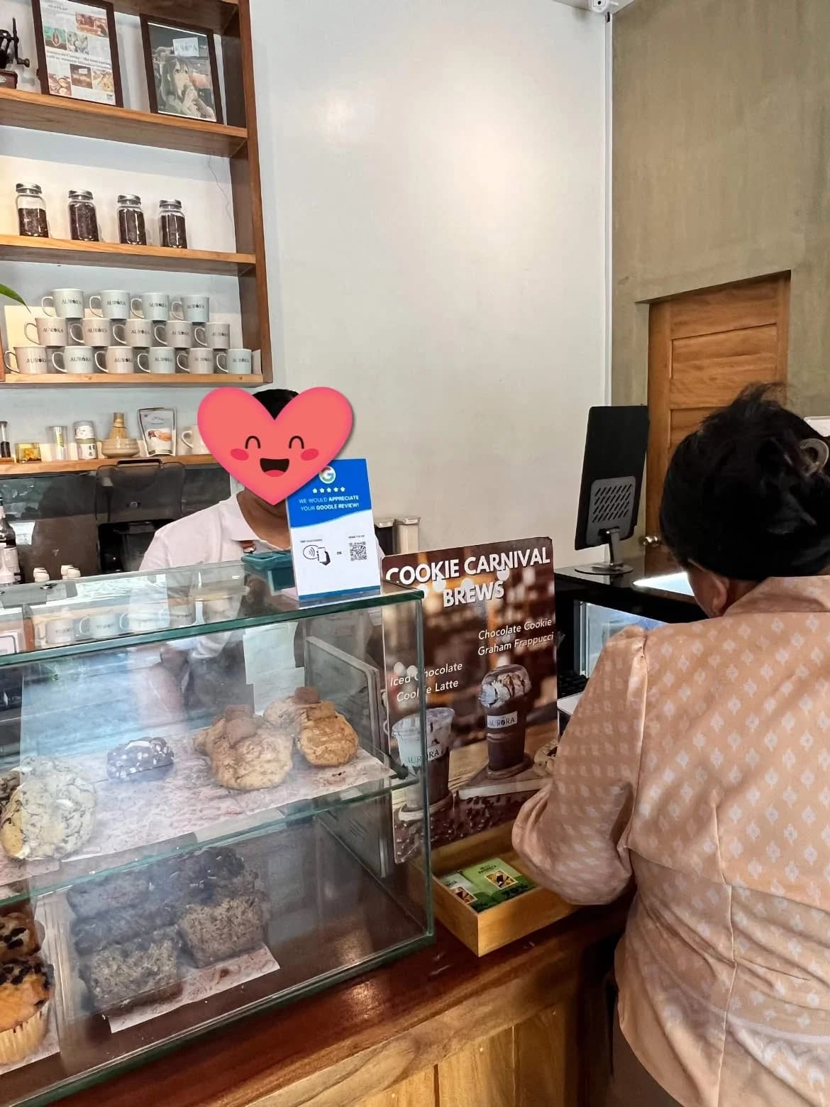 A Goreview stand on a cafe pastry display; the staff member’s face is covered by a heart sticker.